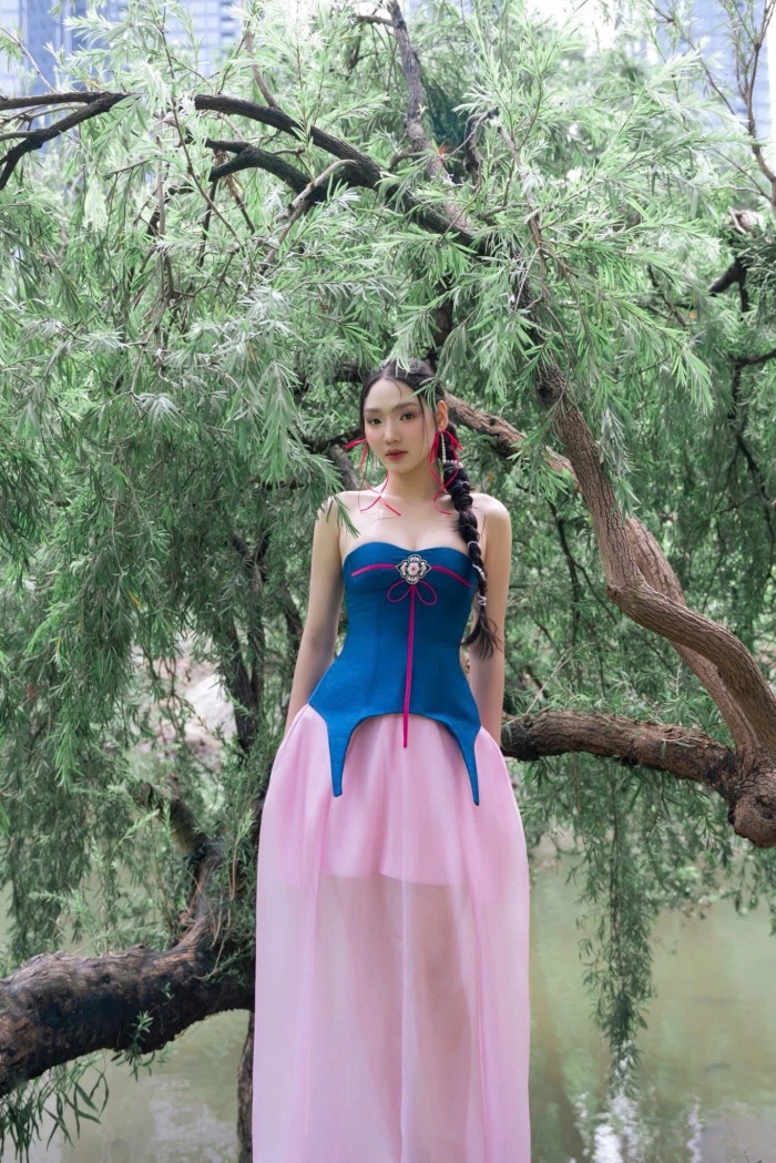 Thay vì dáng áo dài truyền thống, Minh Anh chọn thiết kế cúp ngực hiện đại, giúp khoe khéo bờ vai trần và xương quai xanh thanh mảnh. Điểm nhấn là phần vạt áo được cắt xẻ nhọn hoắt, mô phỏng theo dáng áo yếm hoặc áo chẽn cổ xưa nhưng được làm mới đầy cá tính.