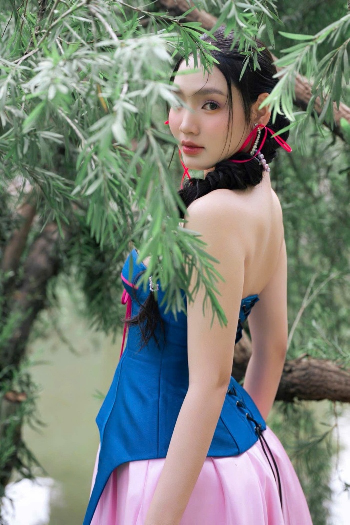 Minh Anh chọn tóc tết lệch một bên, đan xen cùng những sợi dây ruy băng đỏ và trắng mảnh, tạo nên vẻ ngoài vừa ngọt ngào vừa có chút tinh nghịch.