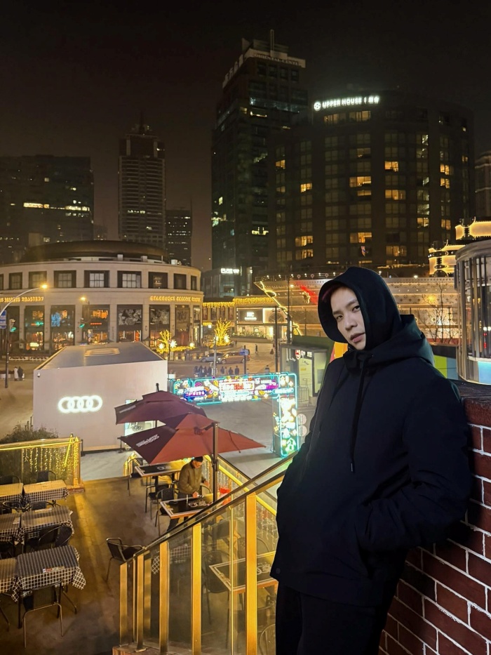 Trong ánh đèn đô thị rực rỡ, nam ca sĩ chọn outfit all-black với hoodie và áo khoác dáng dài. Set đồ mang đậm tinh thần urban, vừa tối giản vừa bí ẩn. Việc sử dụng tông đen xuyên suốt giúp anh nổi bật giữa không gian đầy màu sắc, đồng thời tạo cảm giác trưởng thành và có phần “cool ngầu”.