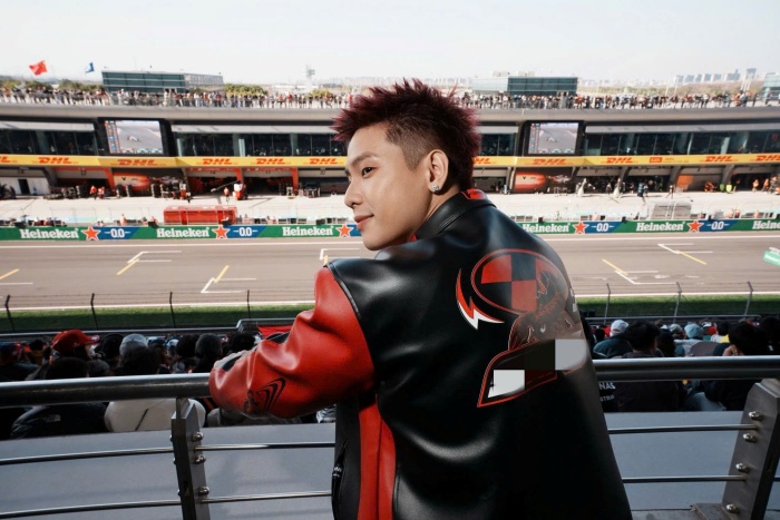 Ngay tại trường đua, nam ca sĩ gây ấn tượng mạnh với outfit mang đậm tinh thần racing. Anh lựa chọn áo khoác da phối hai tông đỏ đen nổi bật, kết hợp cùng kính râm và kiểu tóc nhuộm đỏ bừng cá tính, hòa nhịp hoàn hảo với không khí sôi động của F1, hướng đến tinh thần tốc độ, mạnh mẽ và có phần “nổi loạn”.