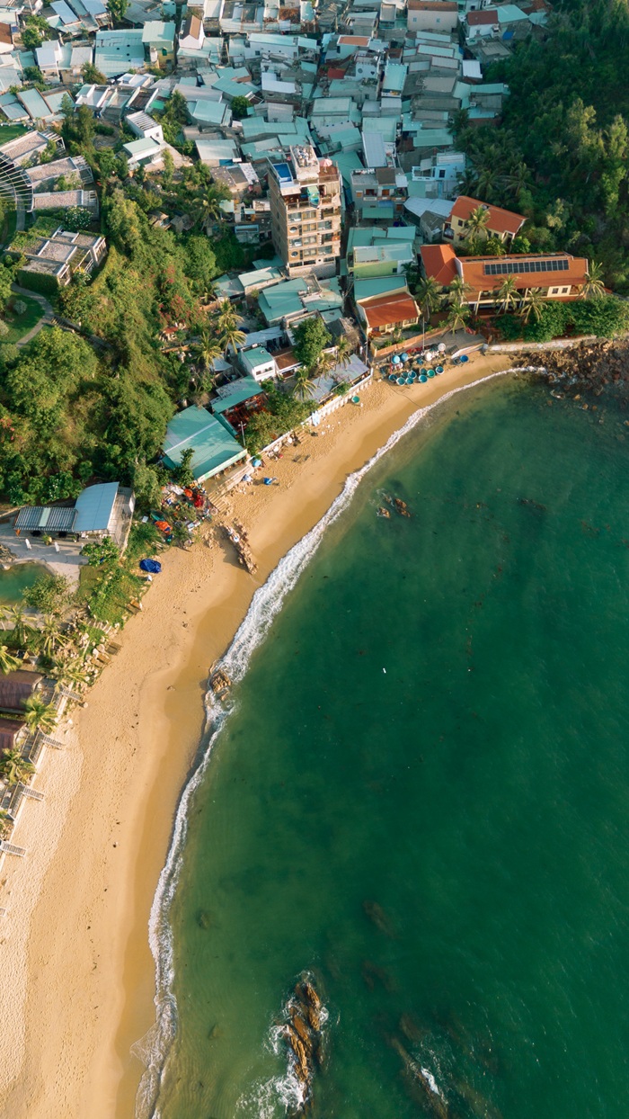 Dải cát vàng ôm lấy làn nước xanh trong, phía sau là khu dân cư ven biển tạo nên bức tranh giao hòa giữa nhịp sống đời thường và thiên nhiên.