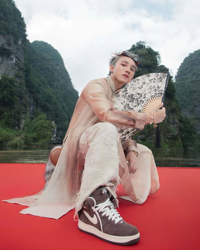 Nam ca sĩ diện áo dài tơ màu be cùng chiếc quần ống suông kiểu cách, phối giày thể thao Nike cùng những phụ kiện như vòng Cartier, Van Cleef & Arpels và quạt Gucci. Ảnh: Instagram nhân vật
